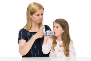 Mother helps daughter inhale asthma spray with spacer