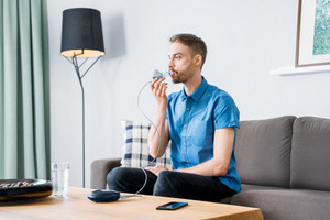Man sits on sofa and inhales with inhalation device