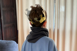 Child from behind with crown on head, scarf around neck and cape