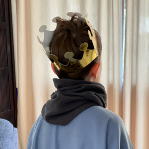 What can be done if a child has mucus in their throat: Scarf Child from behind with crown on head, scarf around neck and cape