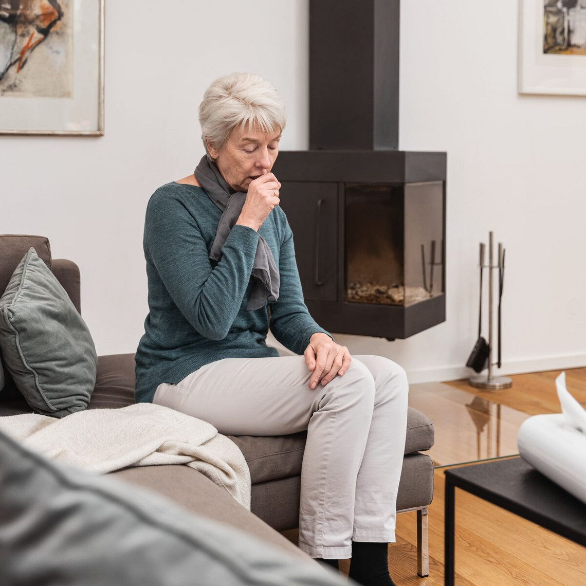 Calming irritated bronchial tubes: This helps manage bronchial symptoms Older woman in the living room, sitting on the sofa and coughing, holding her fist in front of her mouth
