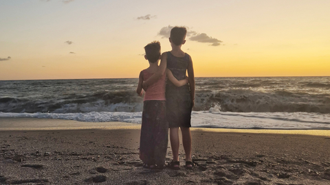 Zwei Jungs stehen am Strand und umarmen sich, Aufnahme von hinten