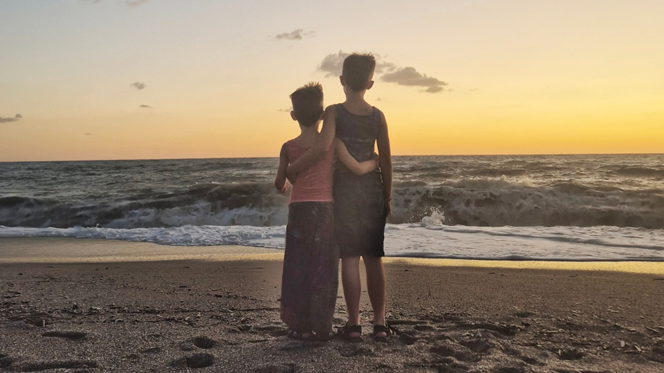 Zwei Jungs stehen am Strand und umarmen sich, Aufnahme von hinten