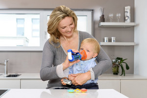 Mother holding baby in one hand, asthma spray with spacer and mask in the other hand