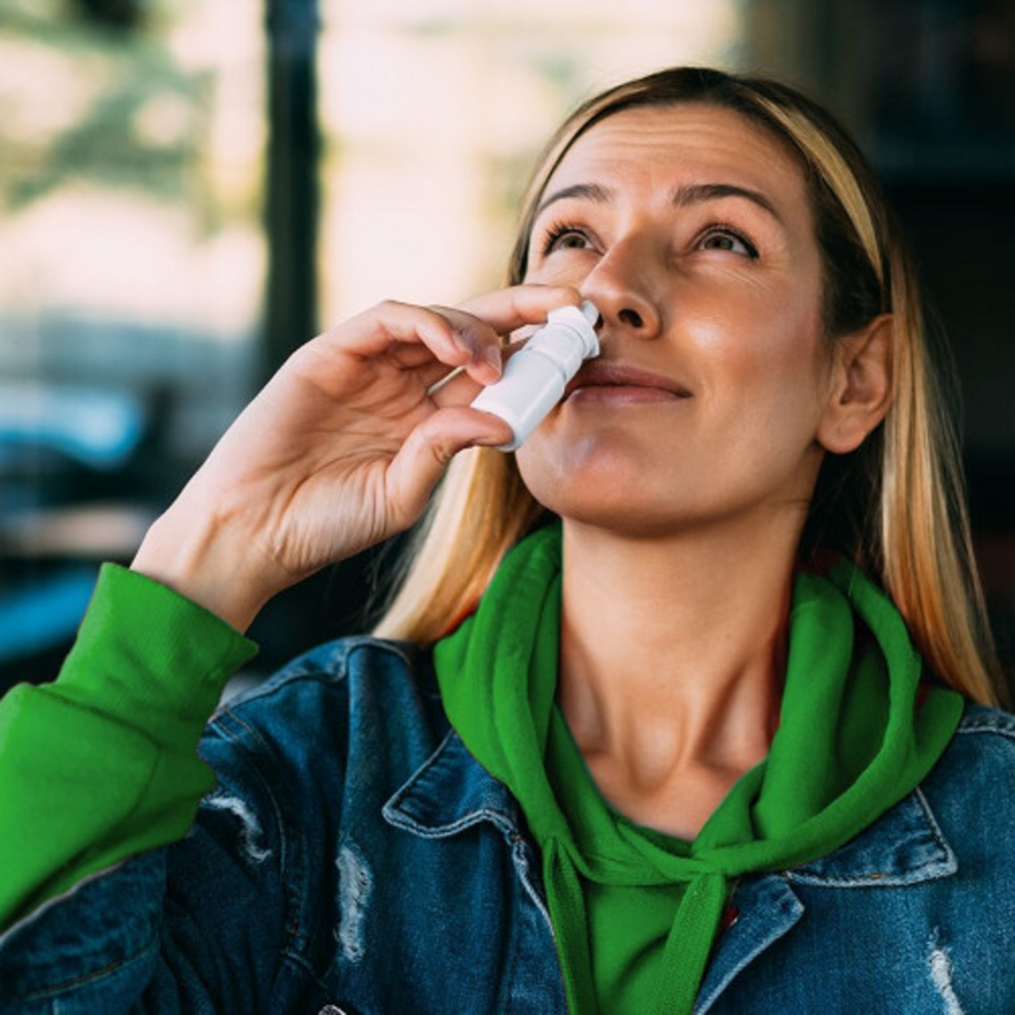 Junge Frau hält sich ein Nasenspray an die Nase