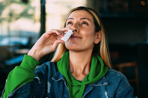 Junge Frau hält sich ein Nasenspray an die Nase