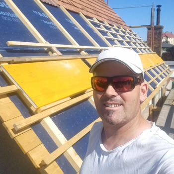 Mann in Halbnahaufnahme mit Cap und Sonnenbrille vor einem halb gedeckten Dach