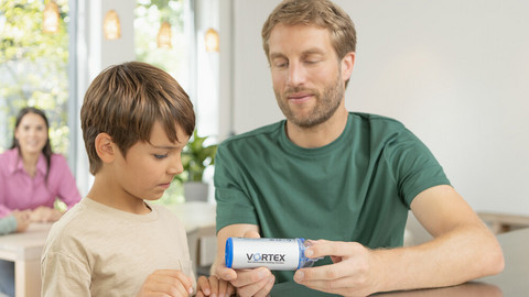 Spacer-Inhalation mit Kindern: Anleitung & das passende Equipment Vater sitzt mit Sohn am Küchentisch und zeigt ihm die VORTEX Inhalierhilfe