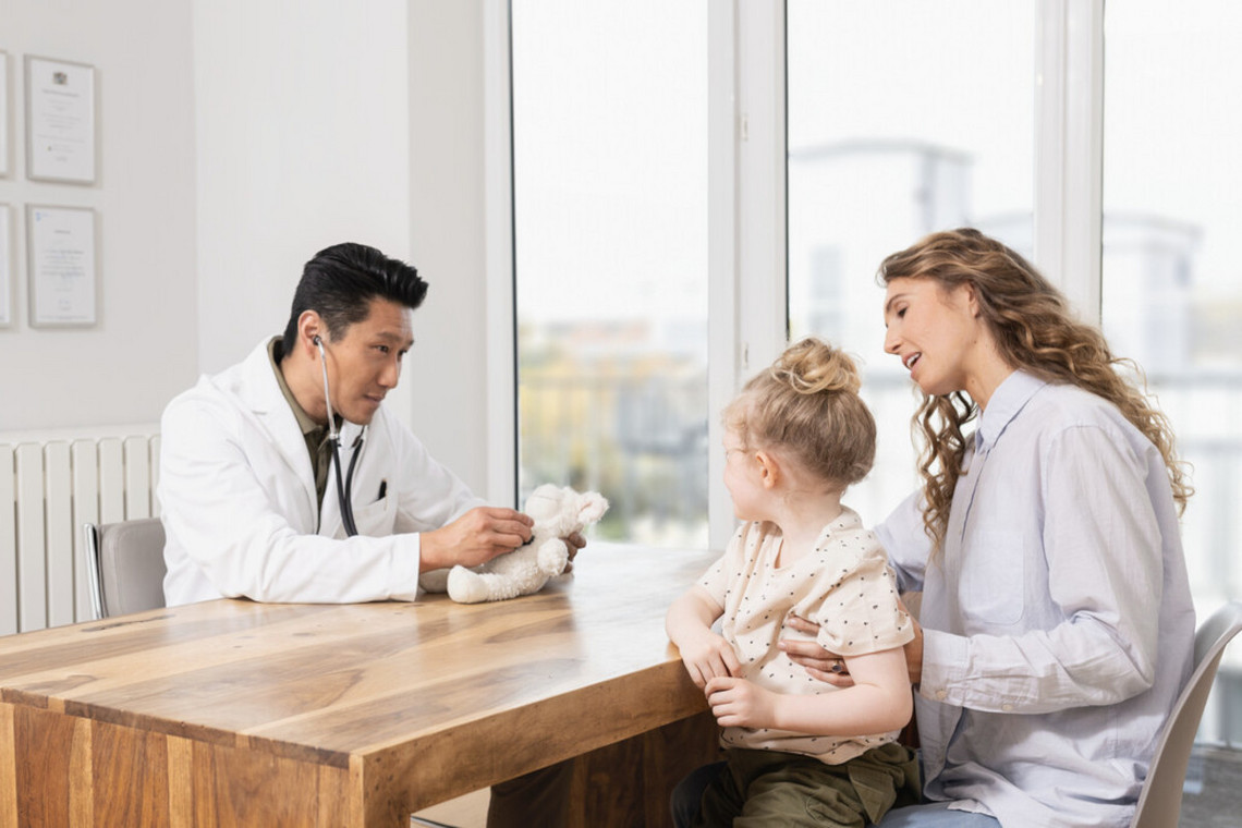 Mother sitting at a table opposite the doctor with her daughter on her lap