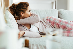 Frau liegt im Bett und hustet in die Armbeuge