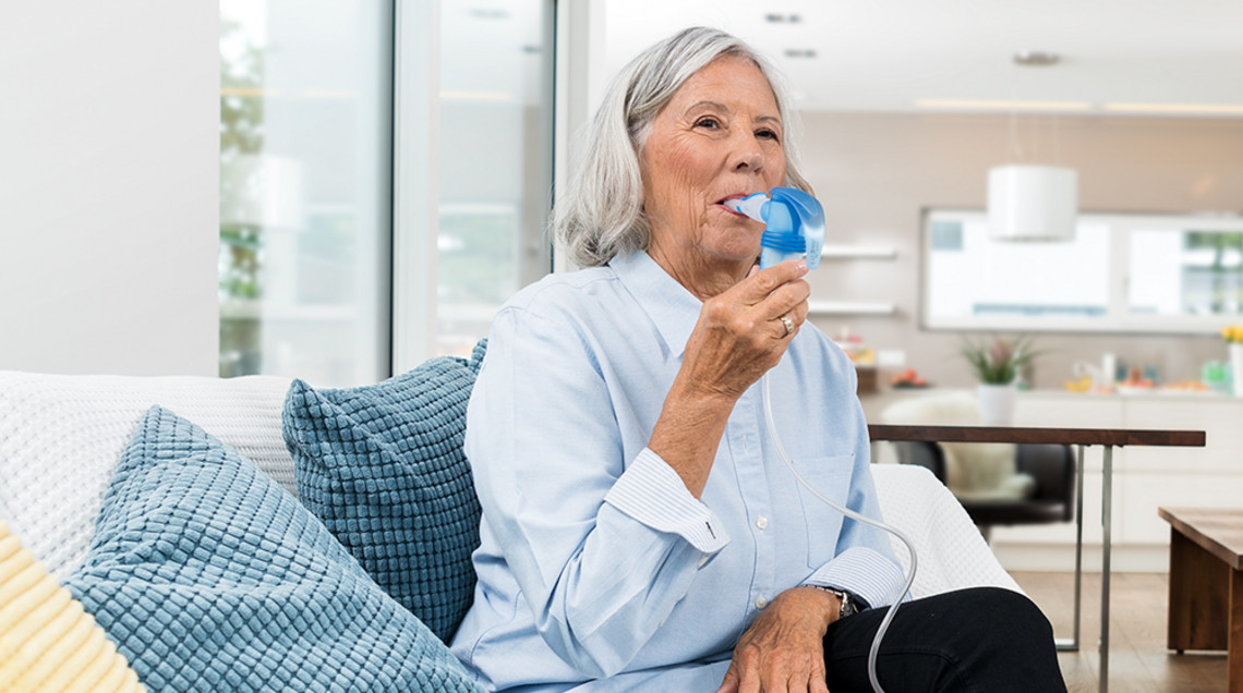 Person using an inhaler while sitting on a sofa at home