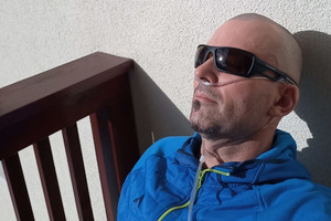 Mann lehnt mit Sonnenbrille und Sauerstoffzufuhr in Nase an der Hauswand 
