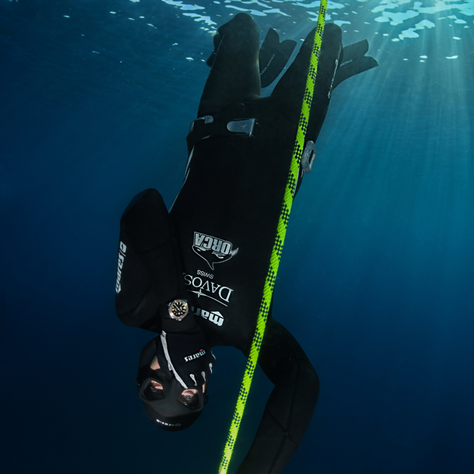 Taucher hängt kopfüber im Wasser, eine Hand hat er an einem Seil, die andere an der Nase