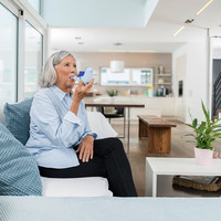 Eine ältere Frau sitzt auf einer Couch im Wohnzimmer und inhaliert entspannt mit dem VELOX.