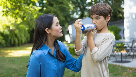 Mother watching son inhaling asthma spray with VORTEX spacer