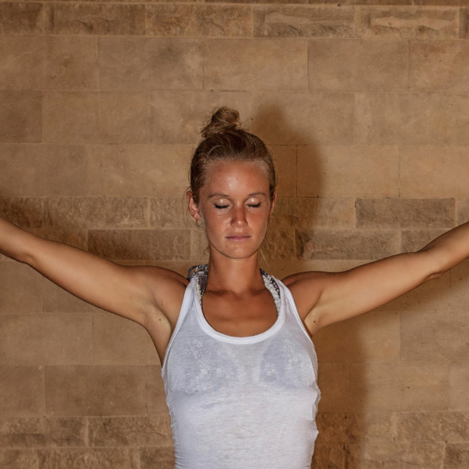 Junge Frau steht mit geschlossenen Augen aufrecht da, die Hände zu beiden Seite ausgestreckt