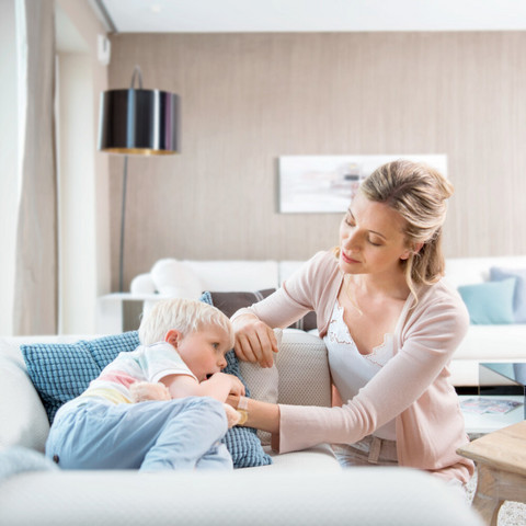 Junge liegt krank auf der Couch, Mutter tröstet ihn