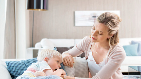 Junge liegt krank auf der Couch, Mutter tröstet ihn