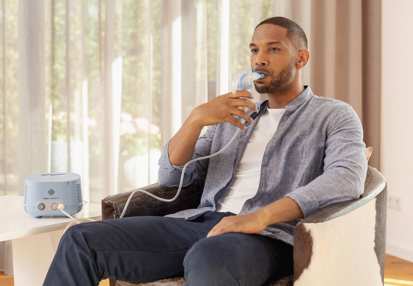 Ein Mann sitzt entspannt in einem Sessel und inhaliert mit dem PARI COMPACT2 Inhalationsgerät.
