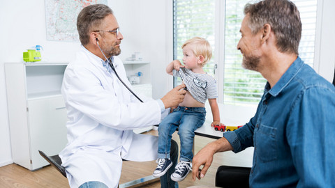 Coughing in children: What can help if your child has a lung infection? Doctor examining little boy with father sitting next to them, watching