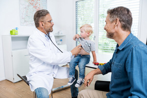 Doctor examines young child with stethoscope while father sits next to them