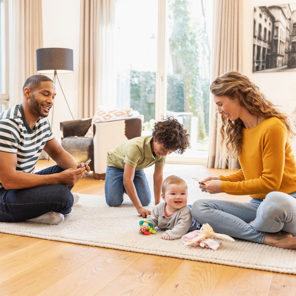 Vater und Mutter sitzen mit ihrem Sohn und ihrem Baby auf dem Teppich und spielen