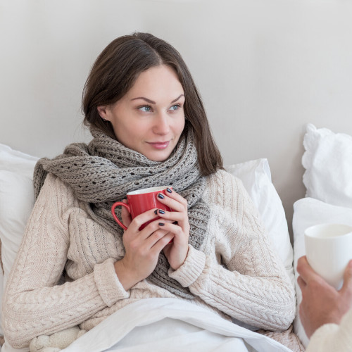 Junge, kranke Frau sitzt im Bett und trinkt Tee