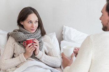 Young, sick woman sits in bed and drinks tea