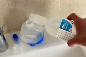 Hand holds nasal rinse and fills it into the tank of the nasal douche