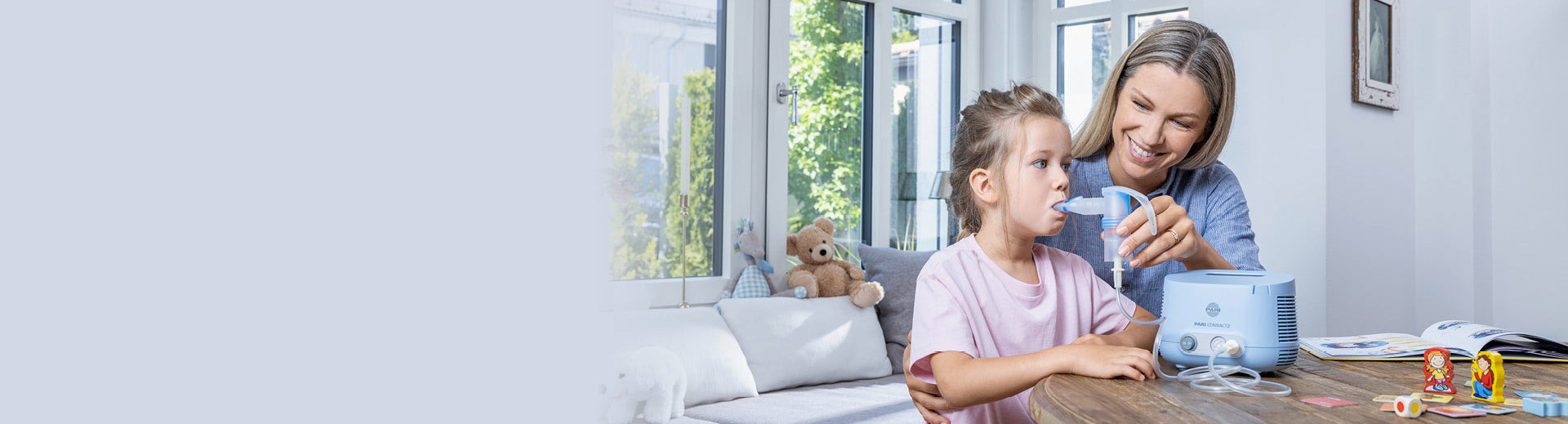 A young mother helps her daughter inhale with a PARI Compact2 inhalation device