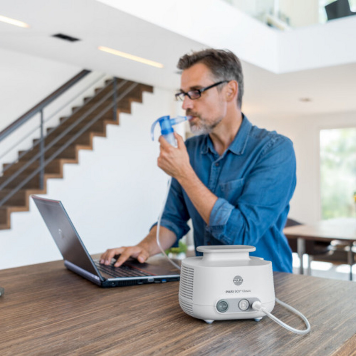 Mann sitzt an Tisch vor Laptop und inhaliert nebenbei
