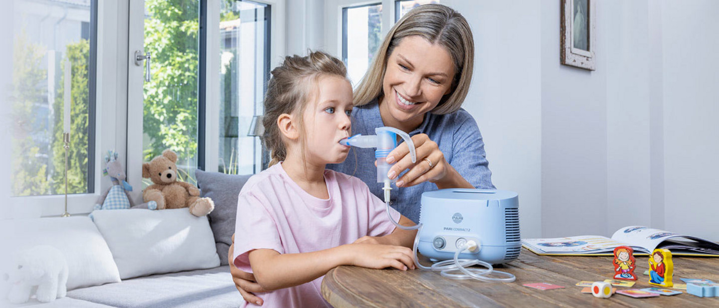 A young mother helps her daughter inhale with a PARI Compact2 inhalation device