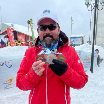 Mann hält in Schneelandschaft vier Medaillen in die Kamera