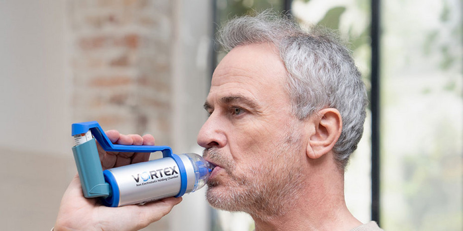 FAQ Inhalation bei COPD: VORTEX Person inhaliert Medikamente mit Asthmaspray und Vorschaltkammer in einem hellen Innenraum.