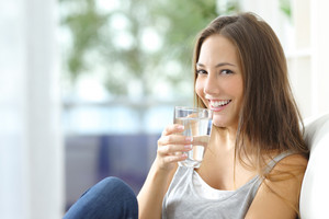 Smiling young woman sitting on the sofa with glass of water in her hand