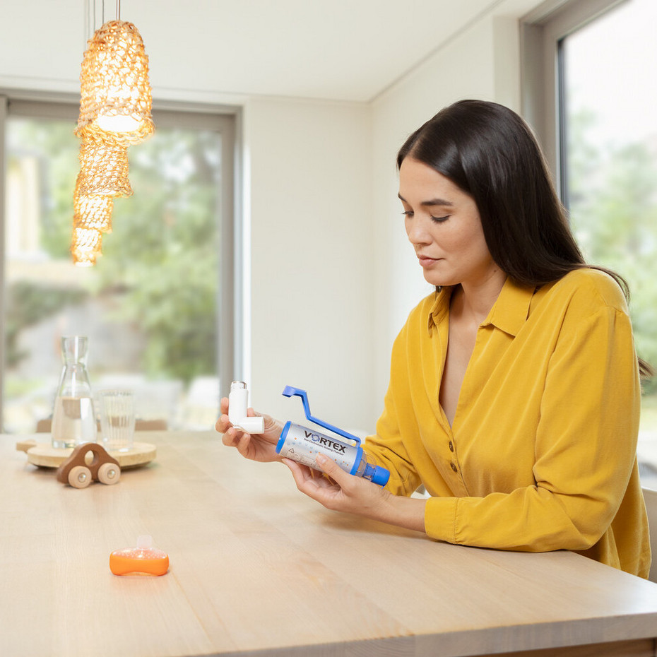 Reinigung der Inhalierhilfe: Spray aus Spacer ziehen Junge Frau sitzt an Wohnzimmertisch und zieht Spray aus VORTEX Inhalierhilfe