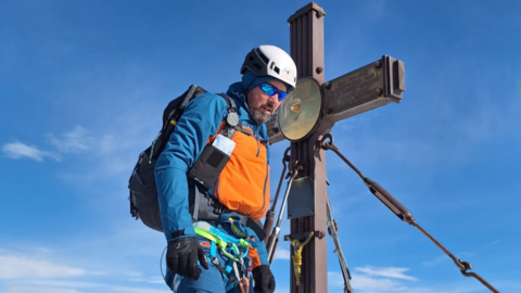 Mann steht an schneebedecktem Gipfelkreuz