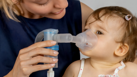 Nahaufnahme von Mutter mit Baby auf dem Schoß, Mutter hat PARI Vernebler in der Hand und hält die Maske vor das Gesicht das Babys