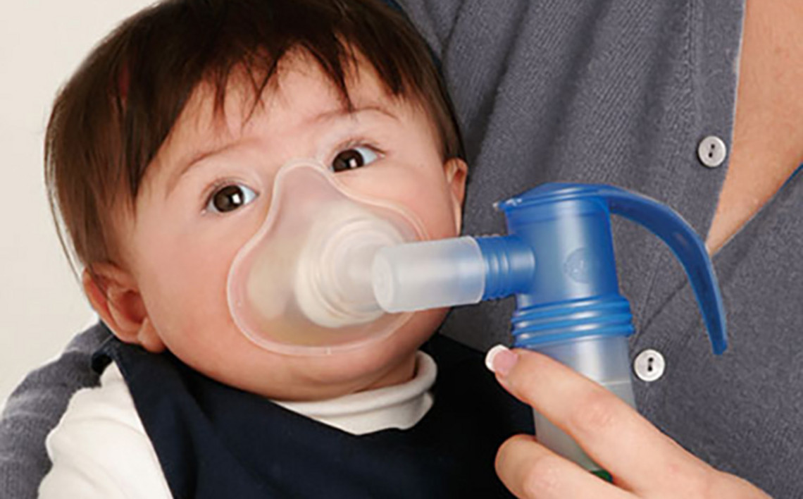 Infant being held while using a handheld nebulizer with a mask for breathing treatment.