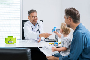 Vater sitzt mit Kind beim Arzt, der ihnen ein Inhalationsgerät zeigt