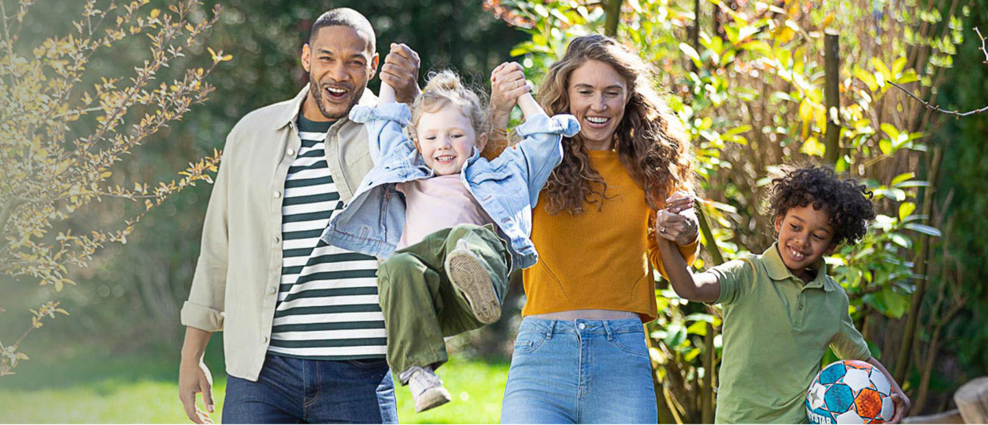 Vater und Mutter heben Kind hoch, zweites Kind an Hand von Mutter