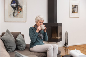 Ältere Frau sitzt auf dem Sofa mit Schal um den Hals und trinke Tee