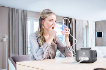 Frau inhaliert am Tisch sitzend mit Inhaliergerät für die Nase