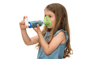 Child inhaling asthma spray with holding chamber and mask