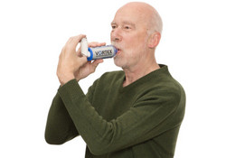 Mann inhaliert aus Asthmaspray mit Spacer
