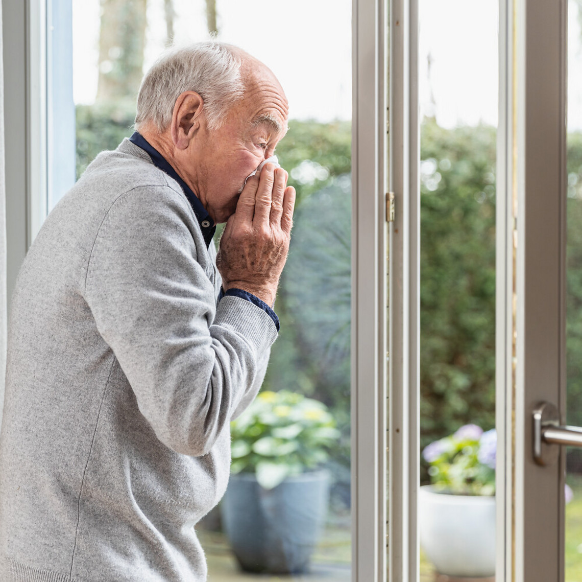 Older man is sniffing his nose while standing at the open window