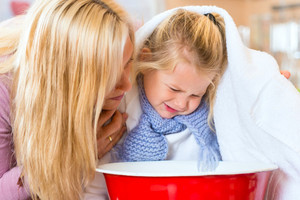 Mutter redet Tochter gut zu, die über einer Schüssel inhalieren soll