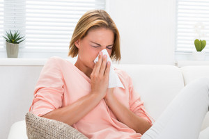 Woman sitting on sofa and snorting into a handkerchief