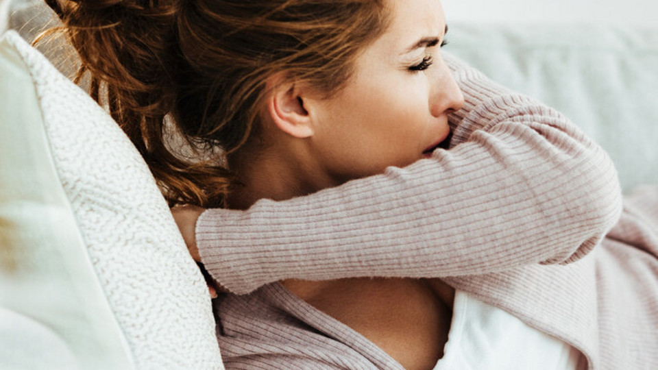 Husten abends und im Bett schlimmer: Warum Asthmasymptome am Abend zunehmen Frau liegt im Bett und hustet in die Armbeuge