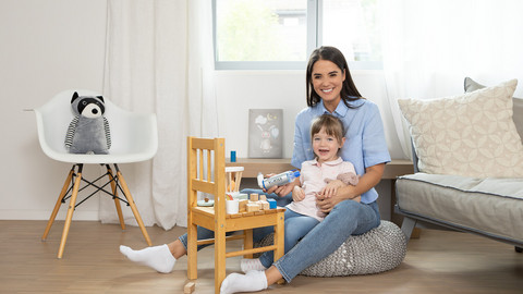 Mutter und Tochter sitzen im Kinderzimmer und lächeln in die Kamera, in der Hand die VORTEX Inhalierhilfe